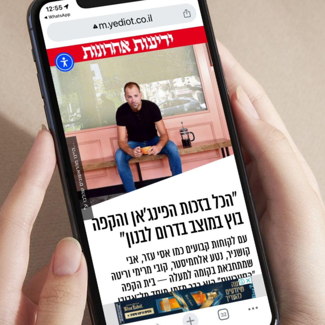 ידיים אוחזות טלפון סלולרי ובו כתבה מידיעות אחרונות על נדב נאמן עם הכותרת: "הכל בזכות הפינג'אן והקפה בוץ במוצב בדרום לבנון"