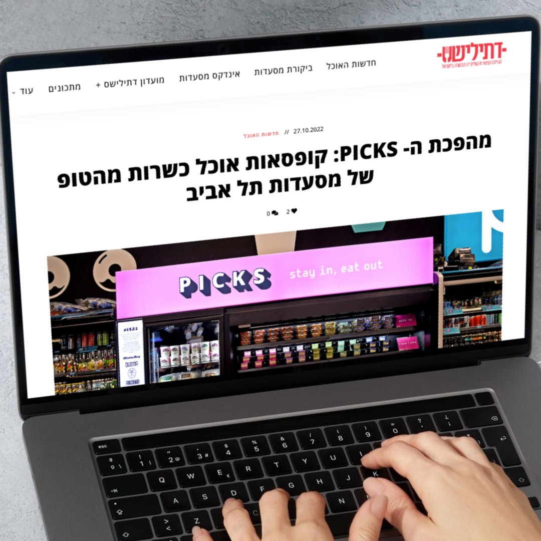 אדם מקליד על מחשב נייד עם כתבת חדשות המוצגת על המסך. כותרת המאמר, הכתובה בעברית, דנה ב"PICKS", קונספט של שירות אוכל בתוך מסעדות תל אביב. המאמר כולל תמונה של מכונה אוטומטית שכותרתה "PICKS" עם הסיסמה "הישאר בפנים, תאכל בחוץ.