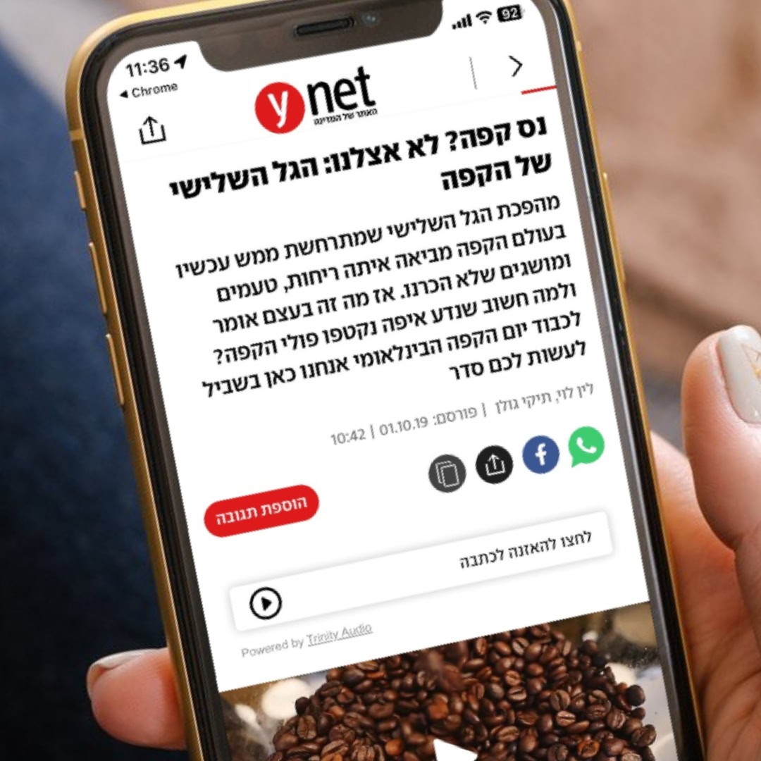 אדם אוחז בסמארטפון המציג דף אינטרנט מ"ynet" עם טקסט בעברית. העמוד כולל כתבה על קפה, המציגה תמונה של פולי קפה ואייקונים שונים הקשורים לתרבות המסעדה. הטלפון מציג את השעה ב-11:36 ואת סמל החיבור האלחוטי.